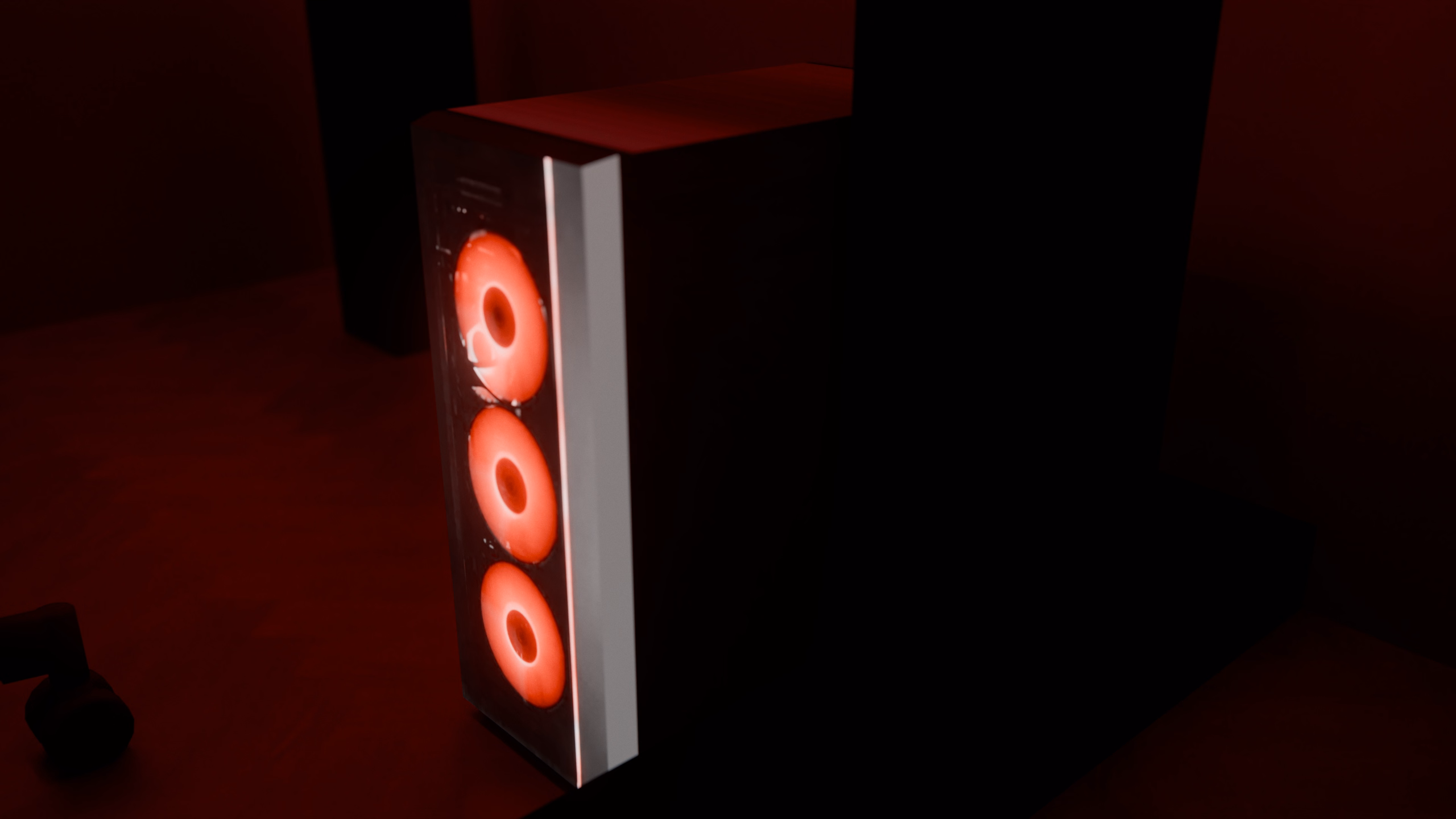 A desktop PC tower with three glowing red fans under the right wing of the desk.